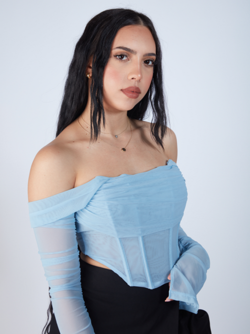 A woman wearing a blue top and black skirt, standing confidently with a poised expression. Baby Blue Corset Crop Top for Women. Boning Corset Style Trends, Doubled lined mesh corset crop top, cute sexy black skirt, gossip girl black skirt style, long wavy beautiful beach hair, how to style long black hair, zade fashion