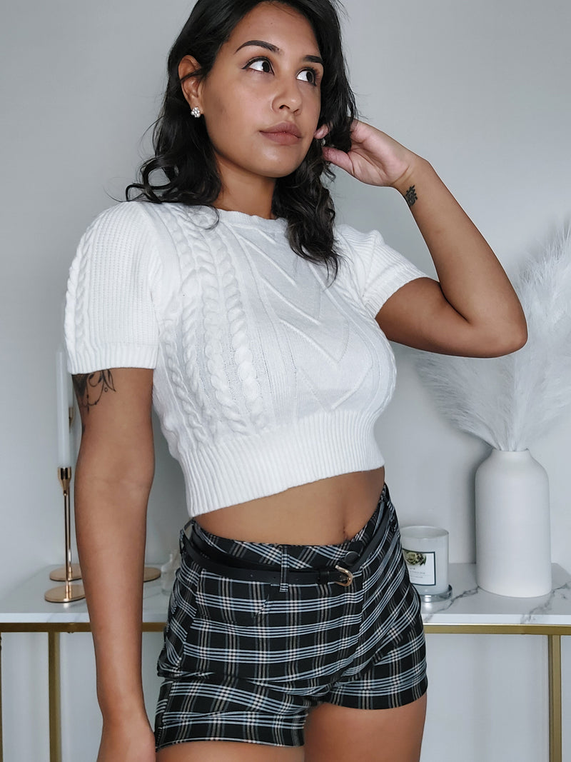 Woman wearing a white cable knit short sleeve crop top with ribbed hem and plaid high-waisted shorts